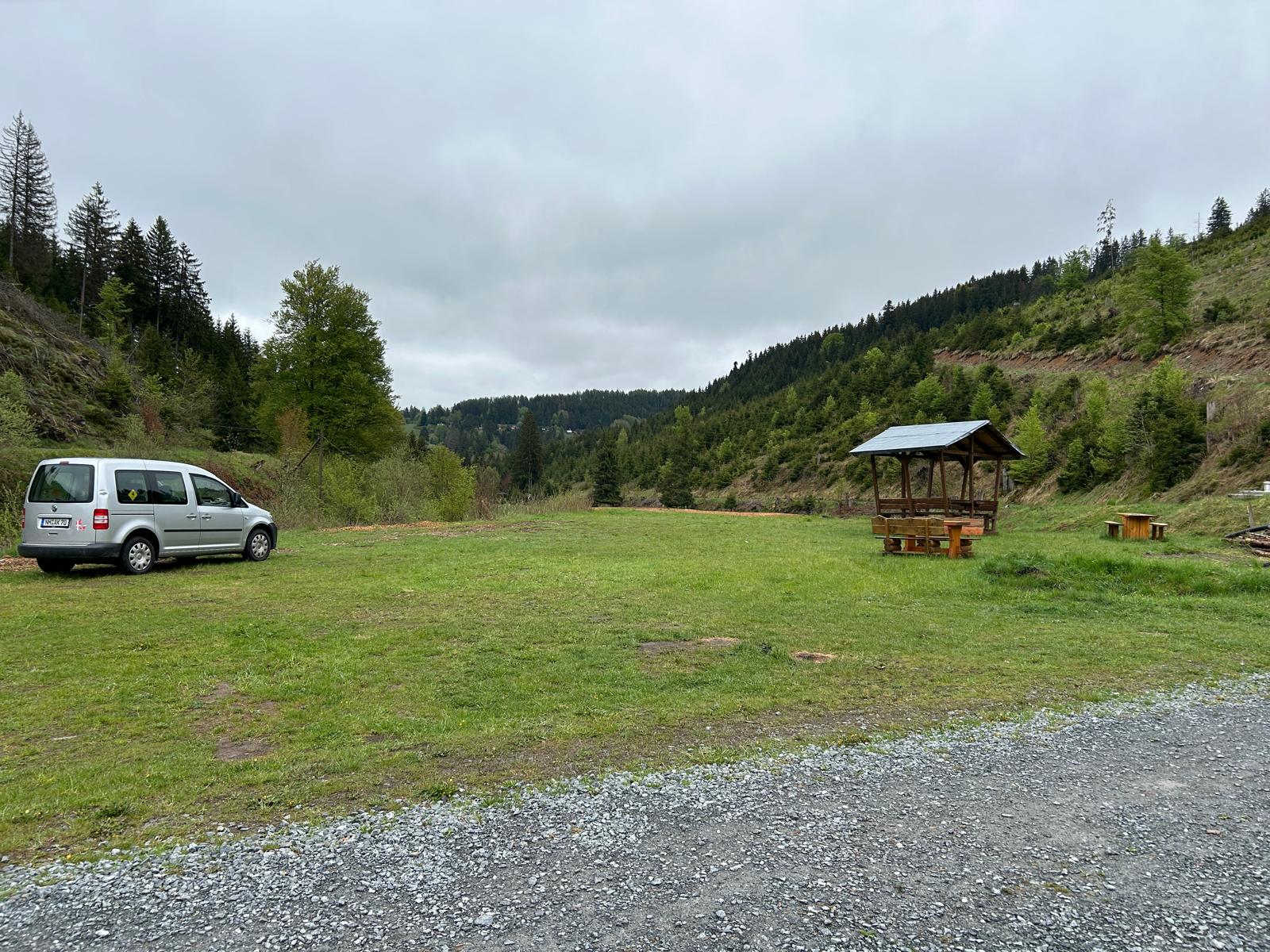 Weite Wiese im Tal mit überdachter Sitzgruppe aus Holz